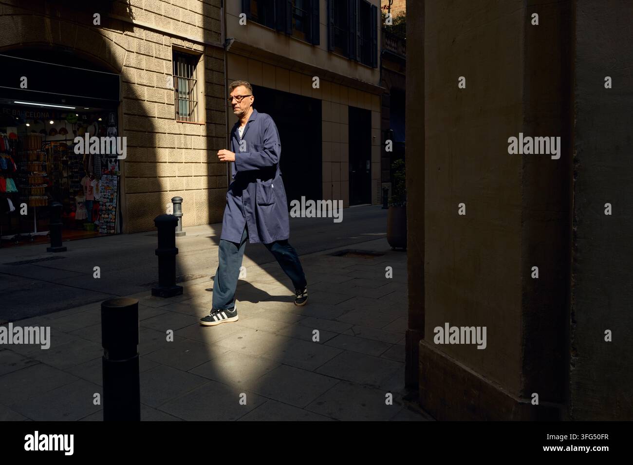 Uomo in giacca da lavoro blu che cammina su una strada cittadina soleggiata Foto Stock