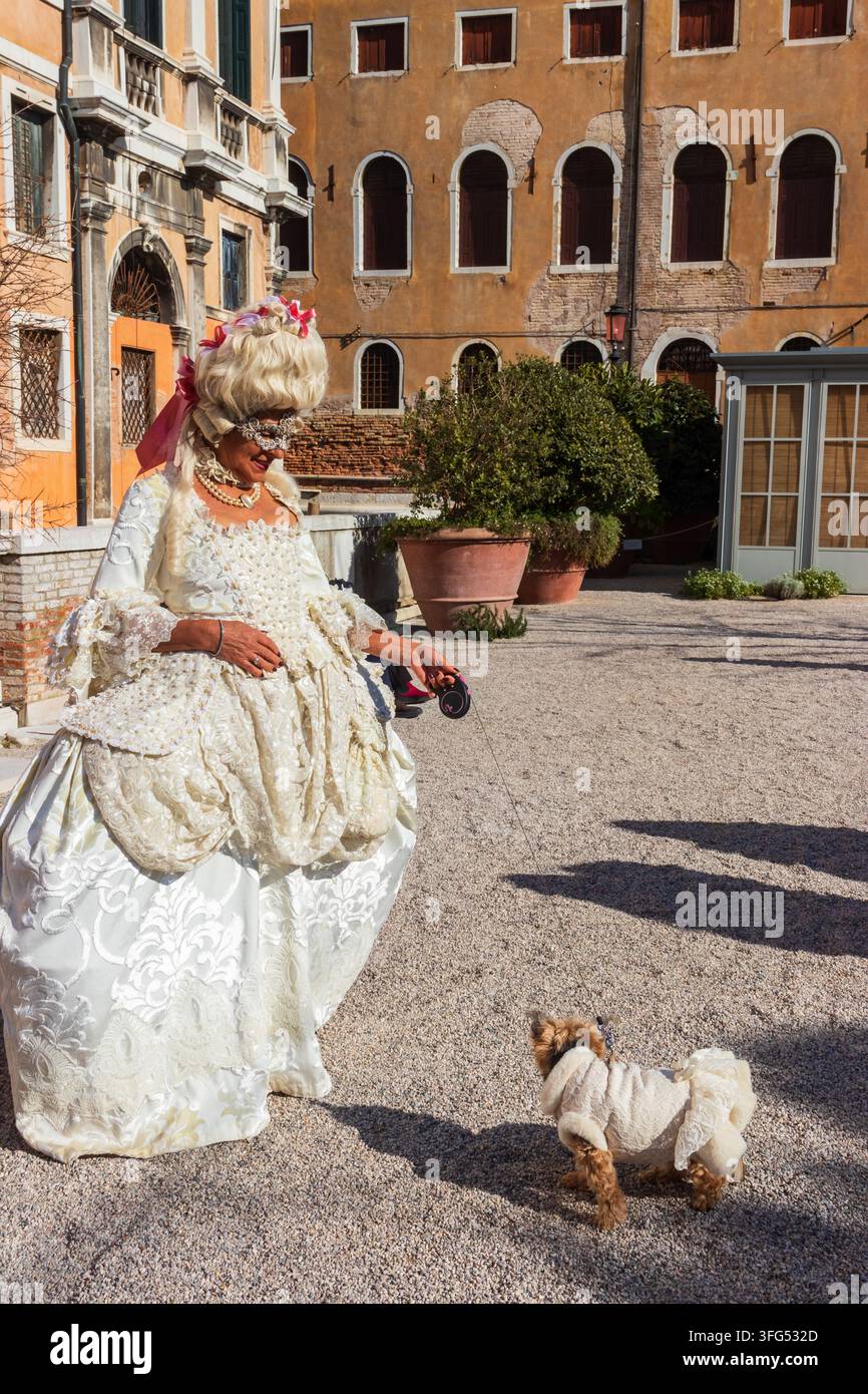Venezia, Italia - 12 febbraio 2023: Ritratto di donna che indossa una maschera bianca e un costume con un cane durante il carnevale annuale di Venezia a Venezia, Italia Foto Stock