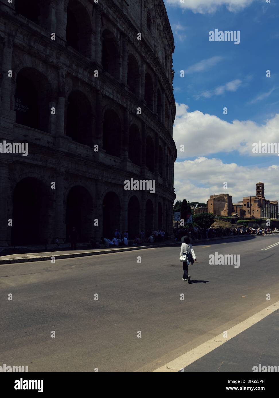 Donna che passa davanti alla massiccia facciata del Colosseo a Roma Foto Stock