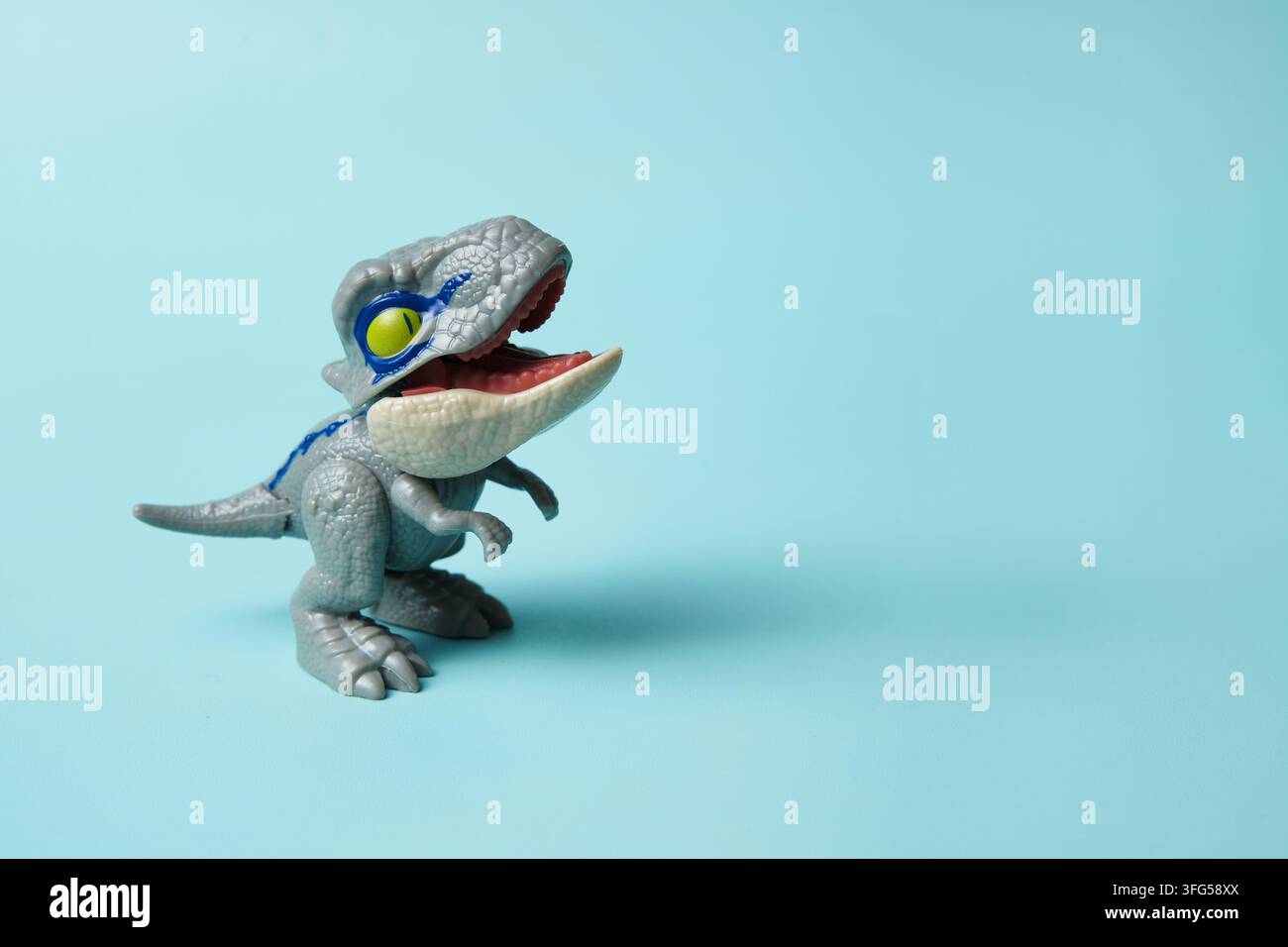 Un giocattolo dinosauro giocoso in piedi su uno sfondo turchese pulito, con la bocca aperta e un'espressione umoristica. Foto Stock