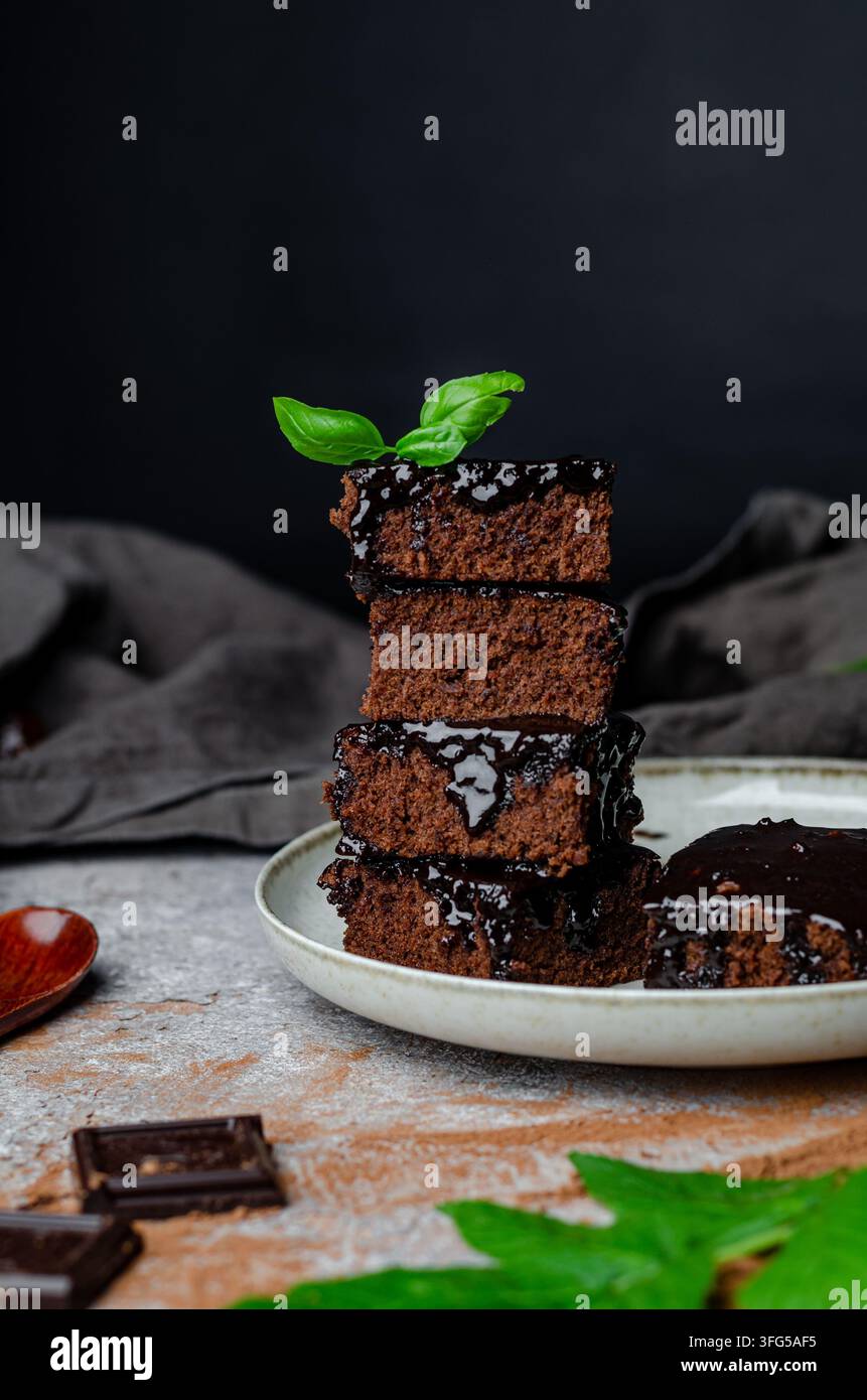Pile di brownies al cioccolato fondente su un piatto di ceramica con basilico fresco Foto Stock