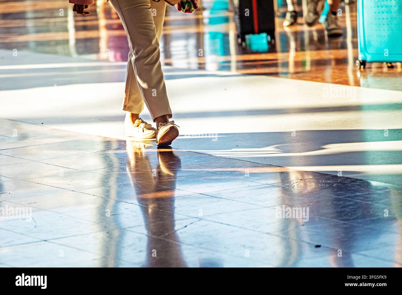 Camminare in pantaloni eleganti attraverso un terminal aeroportuale illuminato dal sole Foto Stock