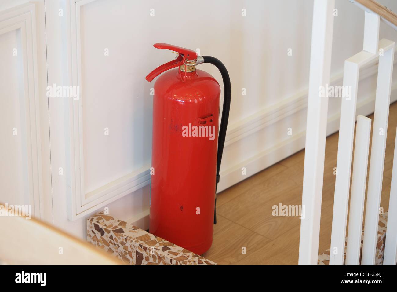 Un estintore rosso è posizionato vicino alle scale in un edificio. È pronto per l'uso.. Foto Stock