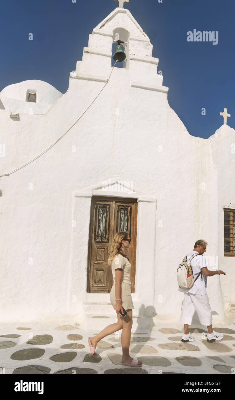 Facciata di chiesa imbiancata a Mykonos, Grecia, con due porte di legno e tetti a capanna gemelli sormontati da croci. Le ombre di due persone sono proiettate Foto Stock