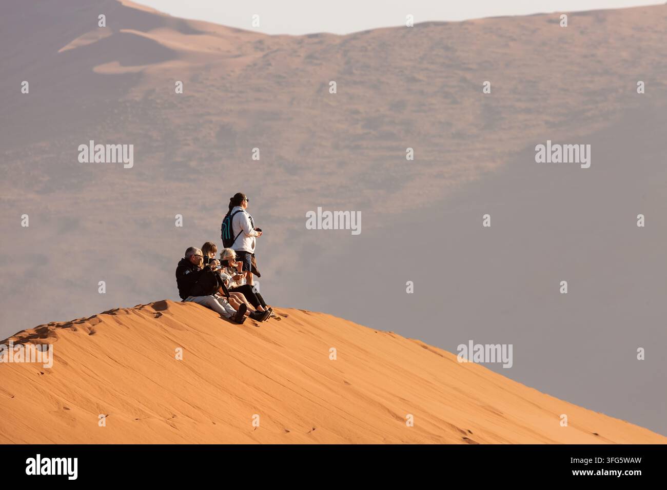 Turisti seduti su una duna di sabbia a Sossusvlei, Namibia Foto Stock