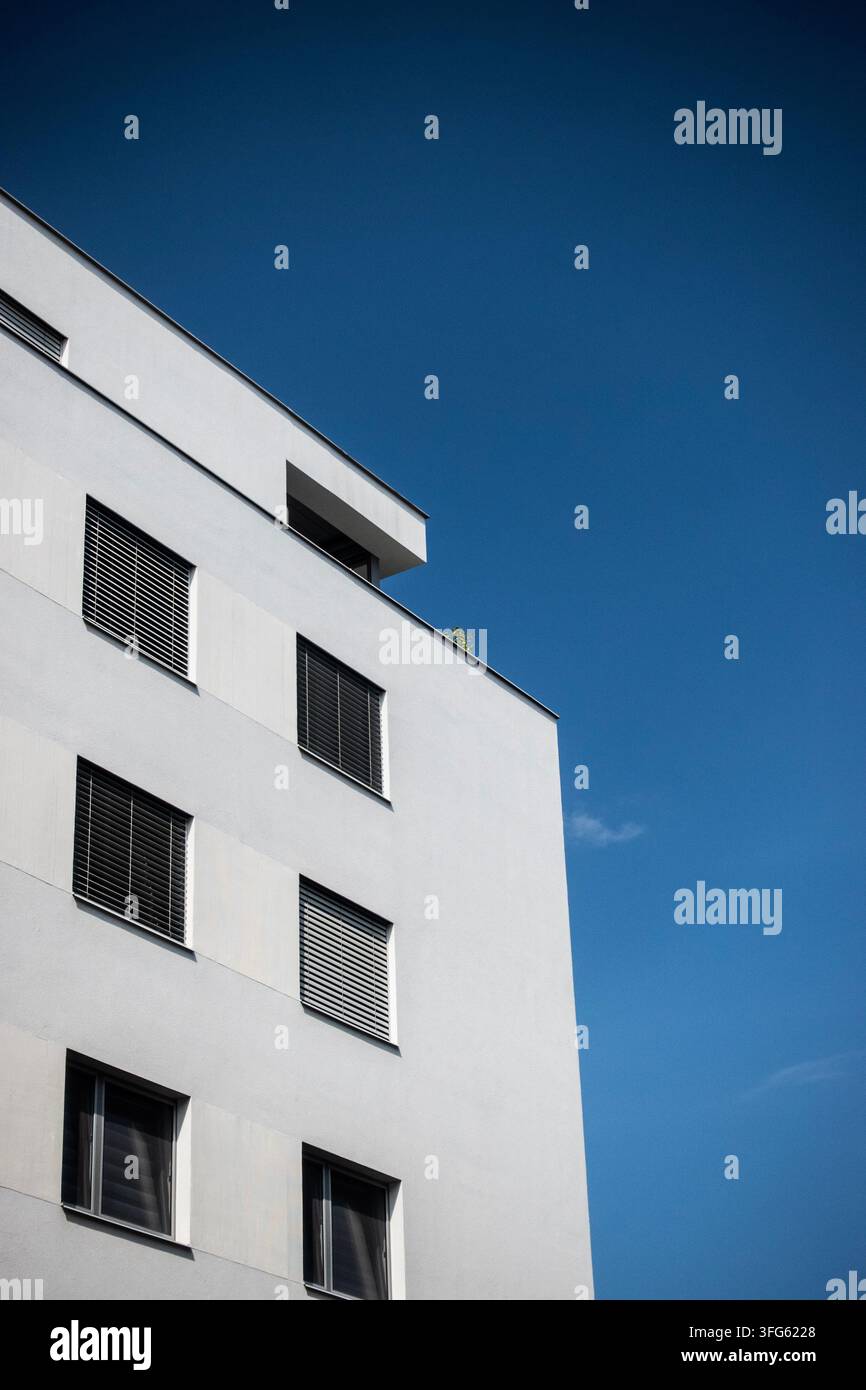 Vista ad angolazione bassa di un moderno edificio residenziale bianco con finestre a persiana su uno sfondo di cielo blu profondo e spazio per testo libero Foto Stock