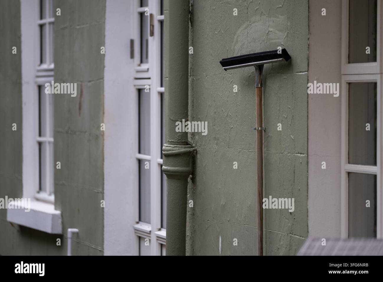 Spazzolino per finestre a manico lungo appeso a un muro esterno consumato accanto a finestre tradizionali. Attrezzature per la pulizia quotidiana e manutenzione della proprietà Foto Stock