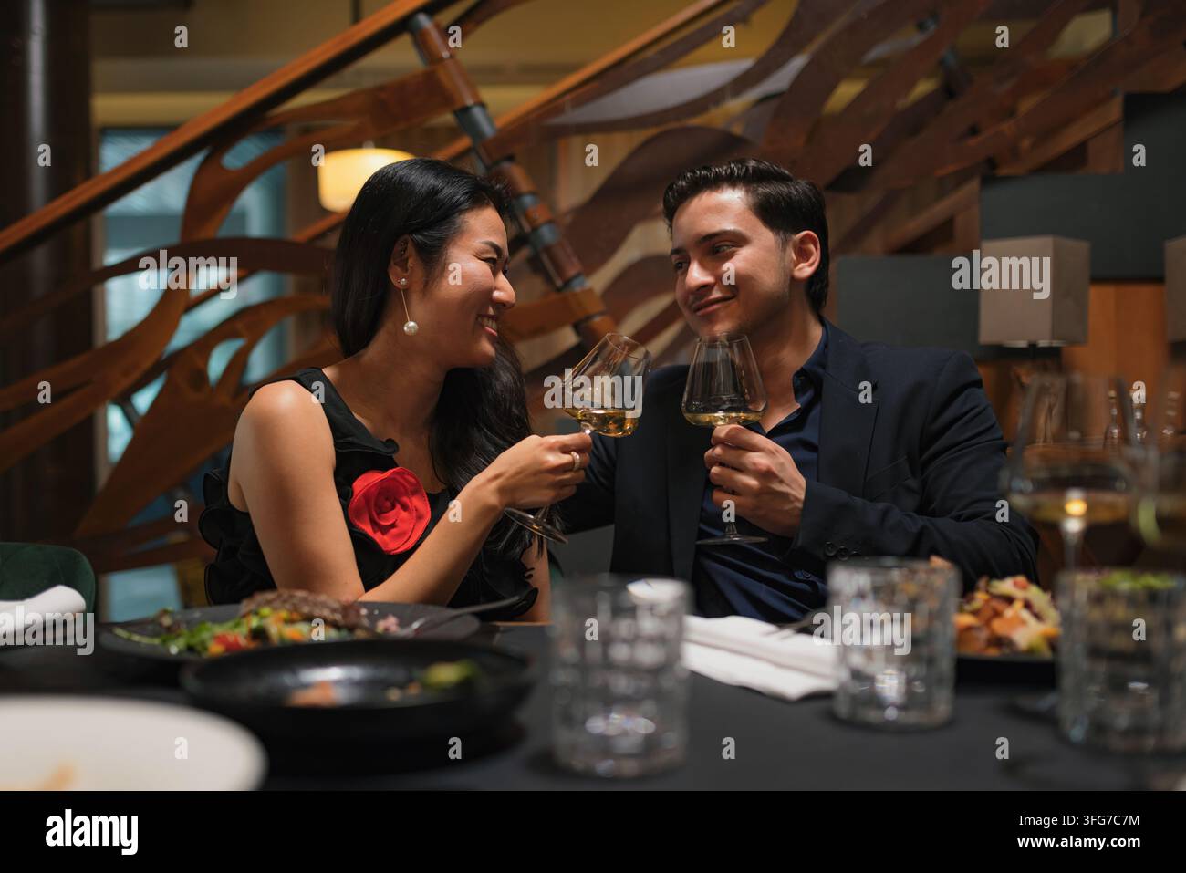 Una coppia felice celebra con un brindisi in un ristorante durante una cena speciale. Si godono la compagnia reciproca con cibo e vino. Foto Stock