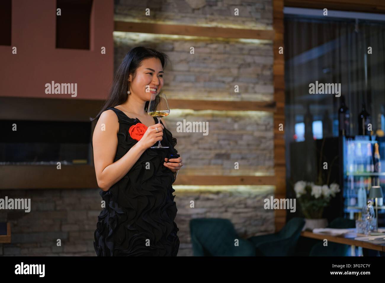 Donna sorride mentre tiene un bicchiere di vino. Le persone intorno a lei celebrano e godono di un'occasione speciale in un ambiente da ristorante. Foto Stock