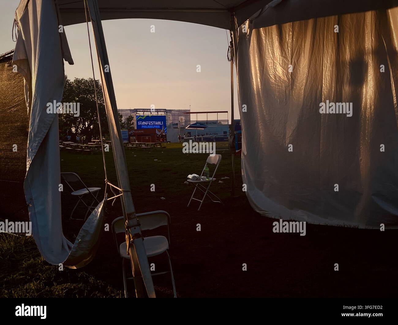 Il sole della sera si posa su un'area festival abbandonata, con un palco vuoto e spazzatura che indugia dopo che la città ha ospitato un successo Fan Festival di 39 giorni - Immagine stock catturata con smartphone