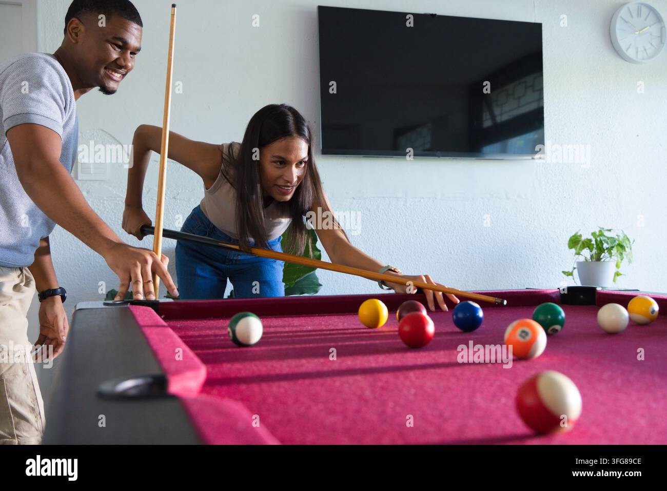 Coppia afroamericana che gioca a biliardo nella sala giochi, donna china, tiene la stecca, palle sul tavolo Foto Stock
