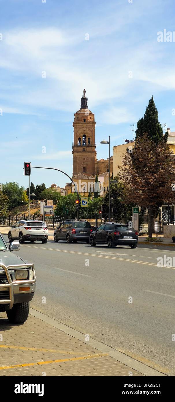 Torre della Cattedrale di Guadix sopra una strada urbana con traffico e alberi. Guadix, Andalusia, Spagna. - Immagine stock catturata con smartphone