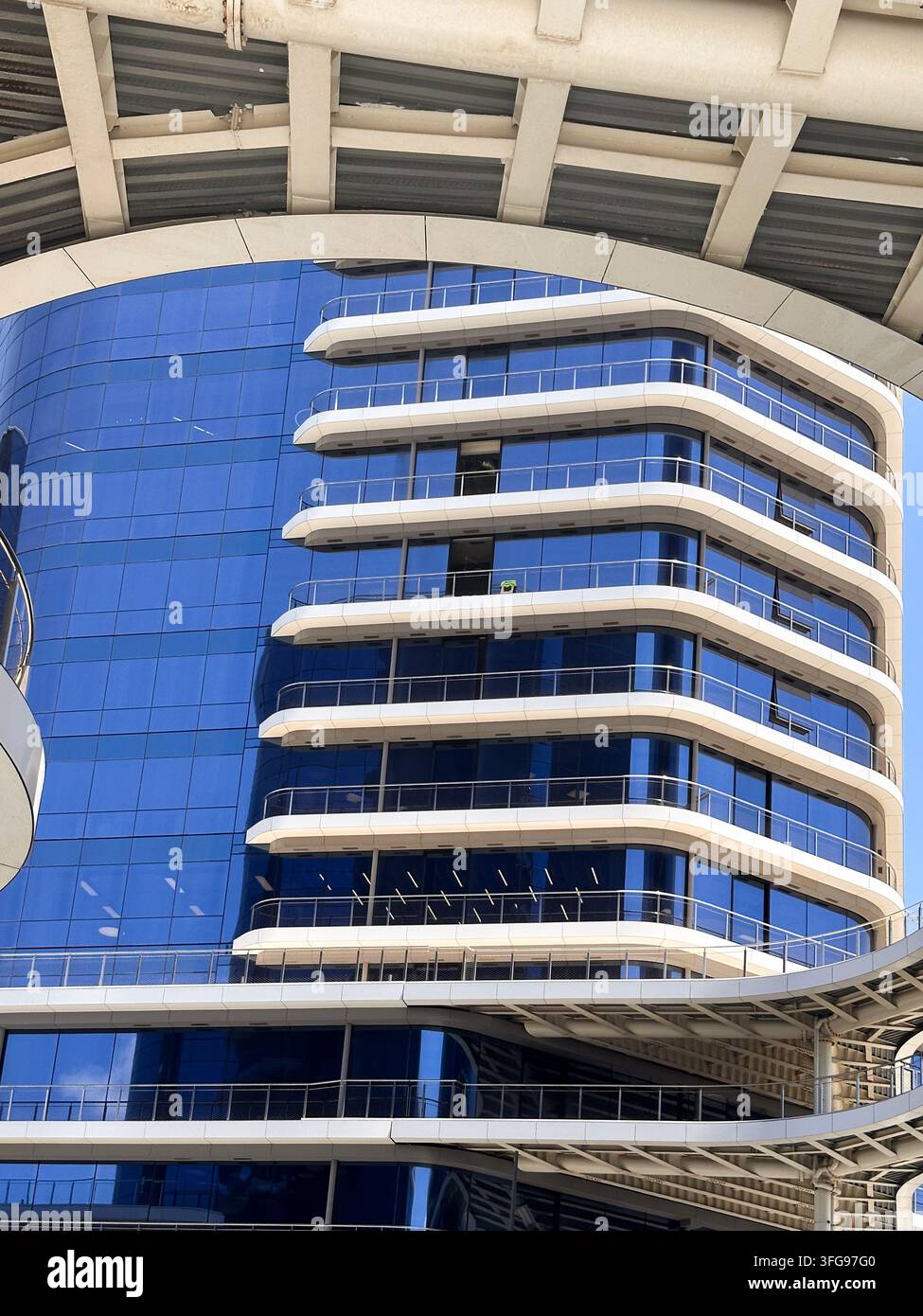 Facciata architettonica contemporanea con vetro blu riflettente, ampie terrazze bianche ed elementi strutturali curvi in un sviluppo urbano moderno Foto Stock