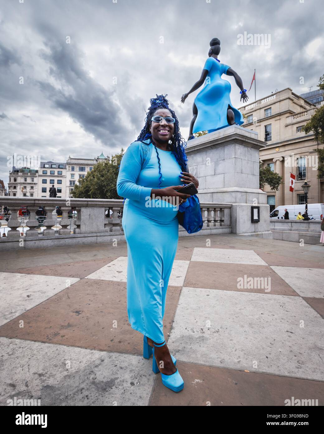 La scultura "Lady in Blue" di Tschabalala Self sul Quarto Plinto di Trafalgar Square a Londra è affiancata da un turista con un abito simile. Foto Stock