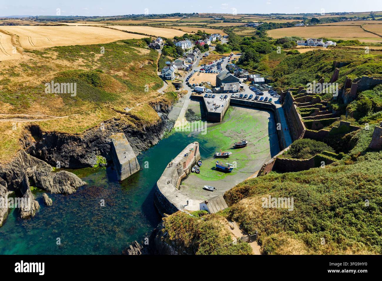 Bacino portuale in pietra storico fiancheggiato da rovine industriali in mattoni, barche da pesca arenate con la bassa marea sotto il sole luminoso dell'estate, prospettiva aerea Foto Stock