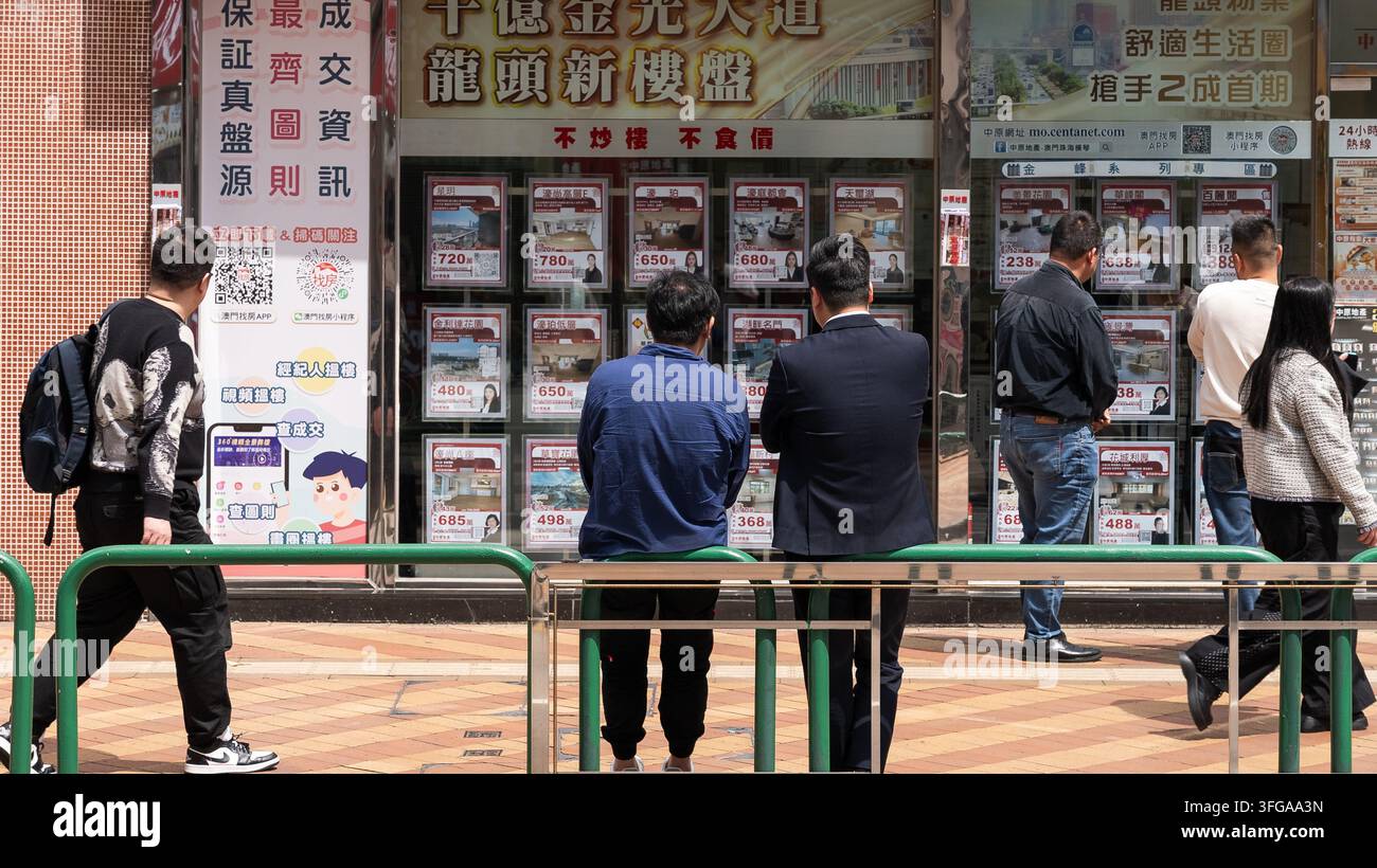 Persone che consultano annunci immobiliari all'esterno di un'agenzia immobiliare a Macau, Cina Foto Stock