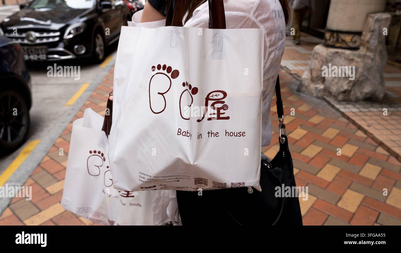 Acquistatore che porta un bambino in sacchetti della spesa del marchio Baby in the House su una strada a Macao, Cina Foto Stock