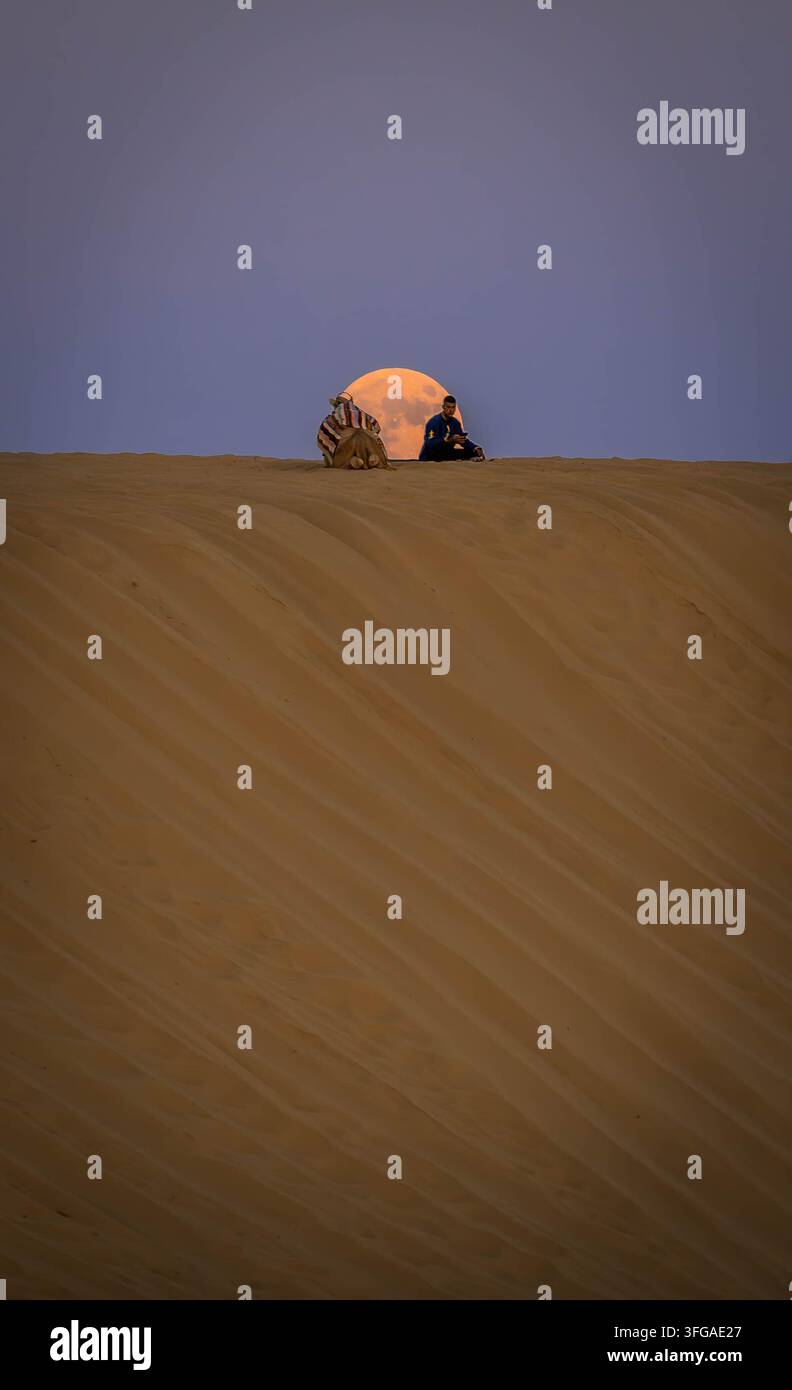 Cammello con uomo arabo seduto sulla duna di sabbia durante il bellissimo tramonto sul deserto del Sahara a Mos Espa, Tunisia. Foto Stock