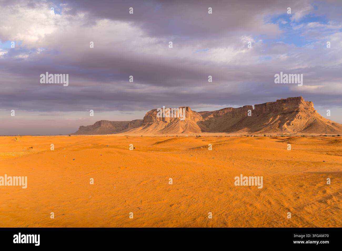 Le dune di sabbia si estendono attraverso il deserto dell'Arabia Saudita verso montagne frastagliate e un insediamento rurale sparso in un vasto paesaggio arido. Foto Stock