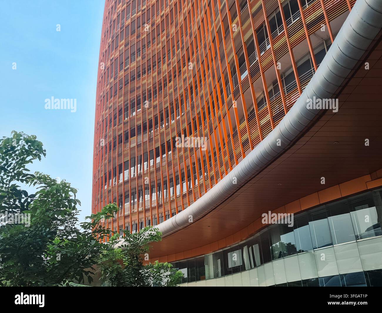 Ripresa a bassa angolazione di un grattacielo arancione moderno con lamelle verticali e architettura curva sotto un cielo blu limpido. Foto Stock
