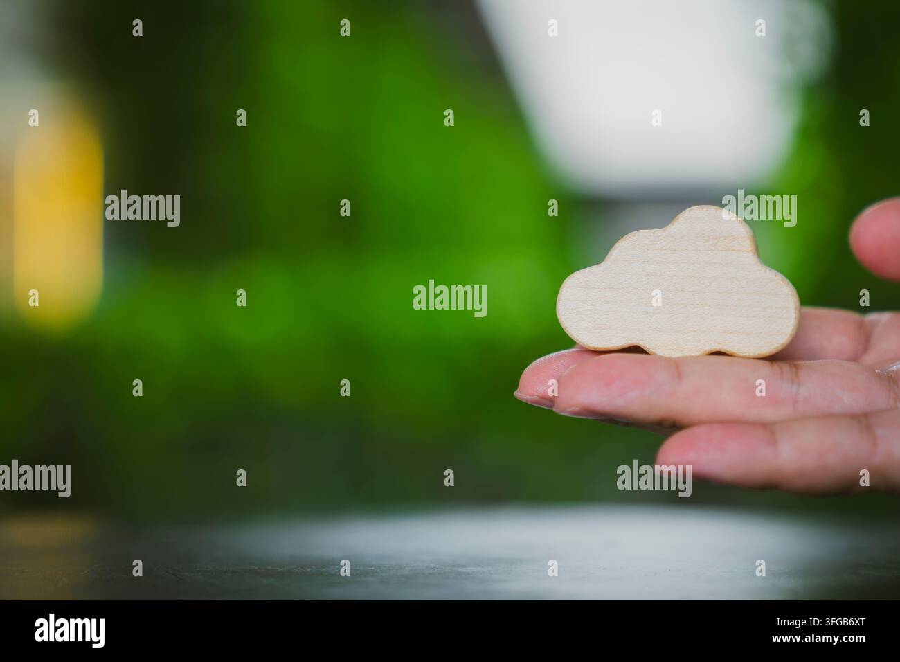 Concetto di cloud computing e IT sostenibile con una mano che tiene un simbolo di legno contro uno sfondo sfocato di natura lussureggiante per lo storage digitale e i dati ecologici Foto Stock