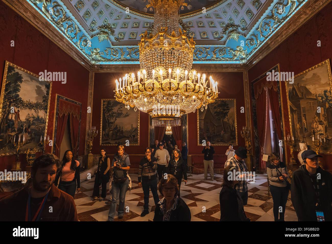 Madrid, Spagna: 7 apr. 2025 – Una folla di visitatori si trova sotto un grande lampadario dorato in una stanza elegante con pareti in damasco tappezzate, adornata da dipinti a olio di ritratti Foto Stock