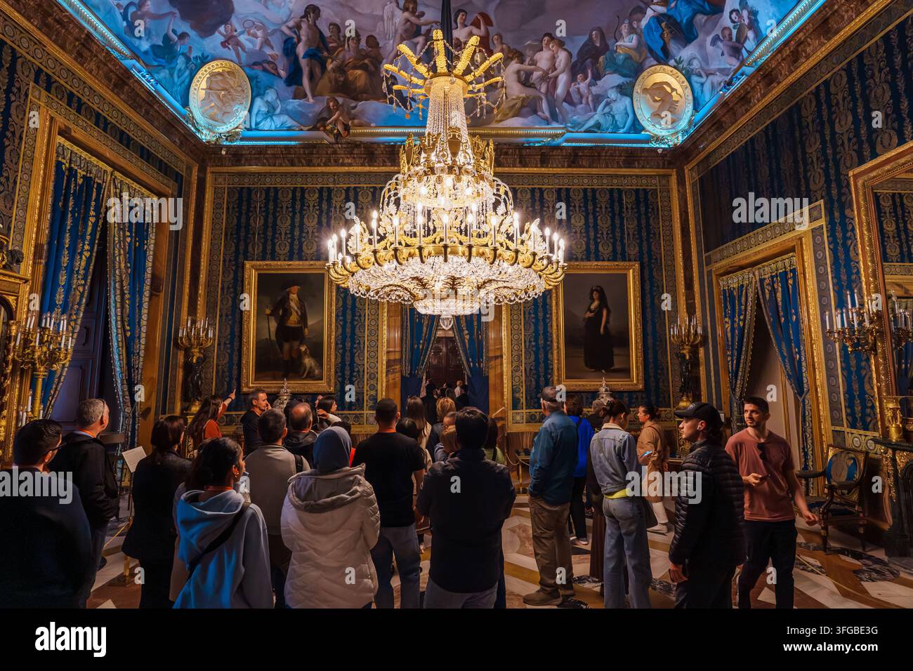 Madrid, Spagna: 7 apr. 2025 – Una folla di visitatori si trova sotto un grande lampadario dorato in una stanza elegante con pareti in damasco tappezzate, adornata da dipinti a olio di ritratti Foto Stock