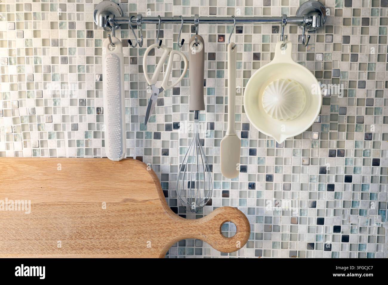 Utensili da cucina appesi a una guida vicino a uno sfondo murale a mosaico. Foto Stock