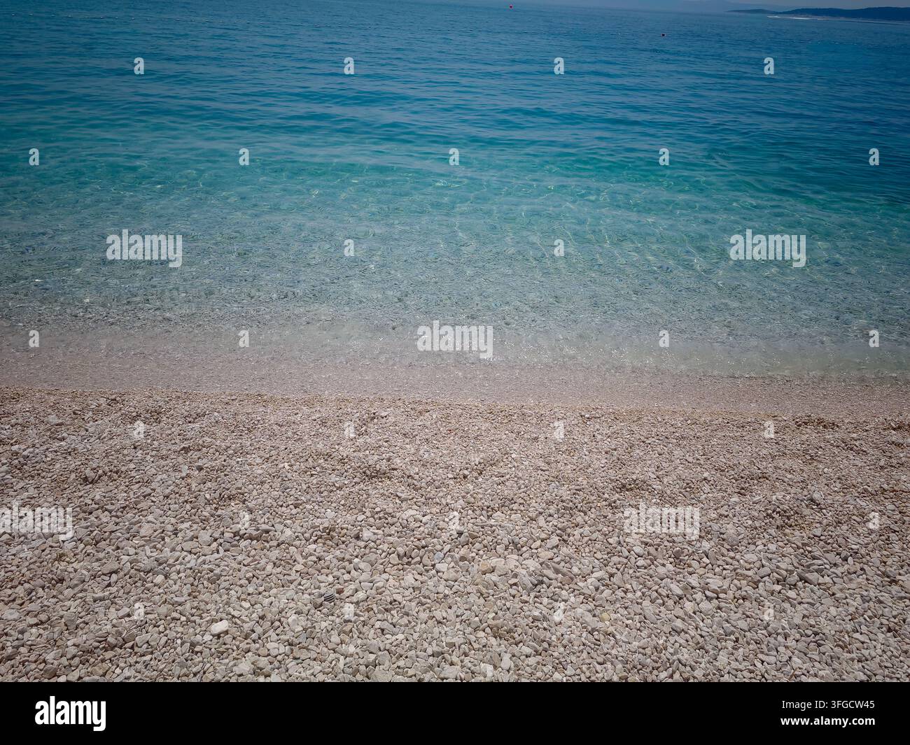 L'acqua di mare cristallina lambisce dolcemente la spiaggia di ciottoli luminosi di Ikovac Beach a Baska Voda, evocando una serenità estiva e una bellezza naturale. - Immagine stock catturata con smartphone