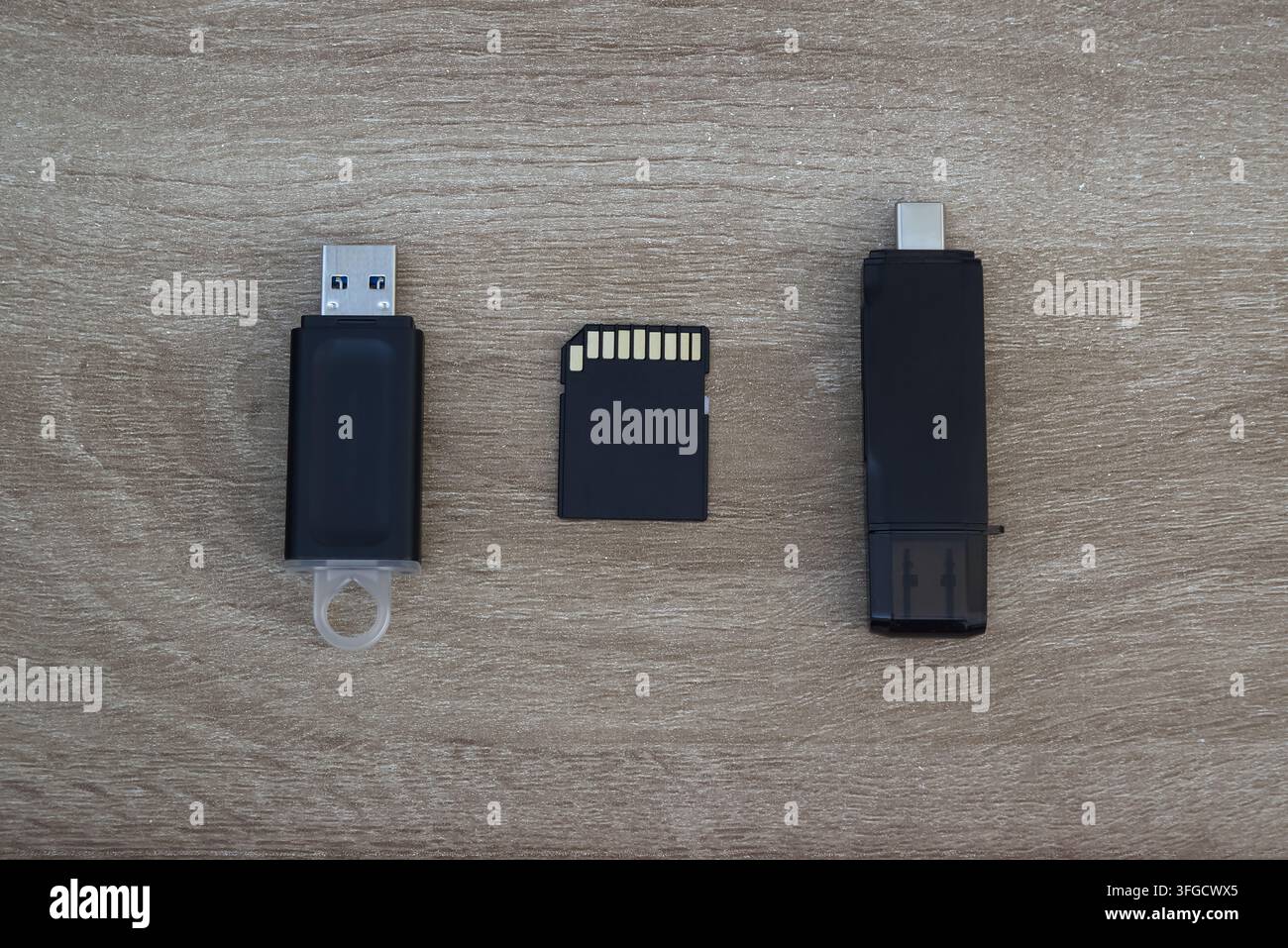 Vista dall'alto di vari supporti di archiviazione digitali tra cui chiavette USB e schede di memoria disposti su uno sfondo in legno chiaro. Foto Stock