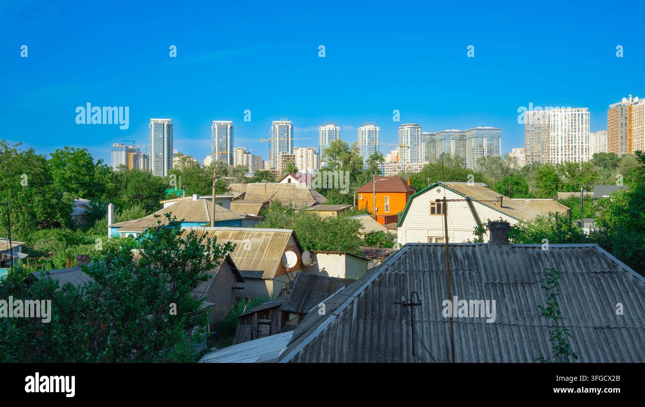 Paesaggio urbano che mostra il contrasto tra vecchie case basse di periferia e moderni palazzi residenziali sotto un cielo azzurro Foto Stock