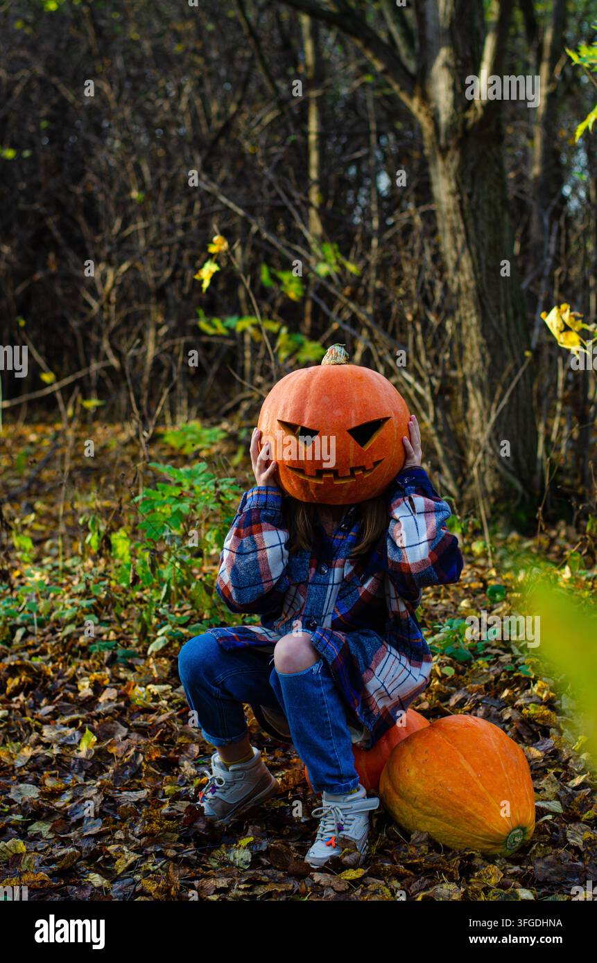 Adolescente seduto su una zucca in una foresta con una testa di zucca, concetto di Halloween Foto Stock