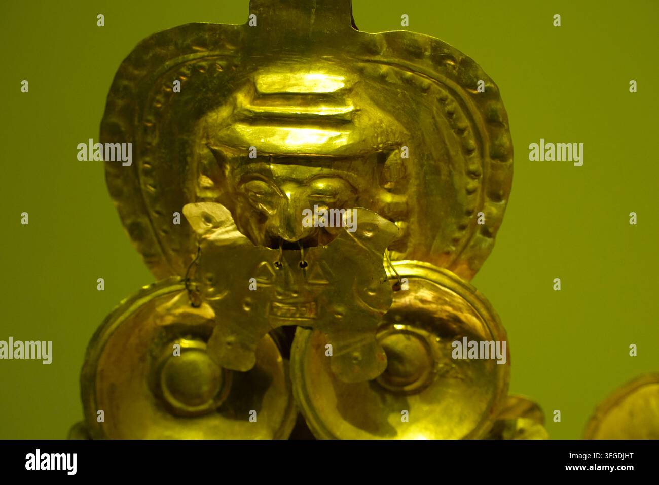 BOGOTA, COLOMBIA - 11 NOVEMBRE 2025: Figura cerimoniale dorata intricata con volto antropomorfo, copricapo e ornamenti pendenti di un periodo precolombiano Foto Stock
