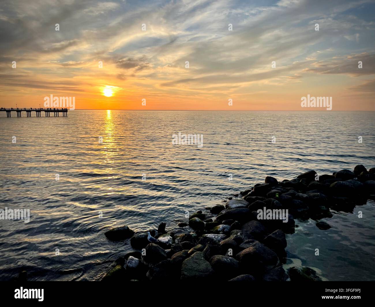 Tramonto sul Mar Baltico con un frangiflutti roccioso in primo piano e il molo di Palanga sullo sfondo a Palanga, Lituania. - Immagine stock catturata con smartphone
