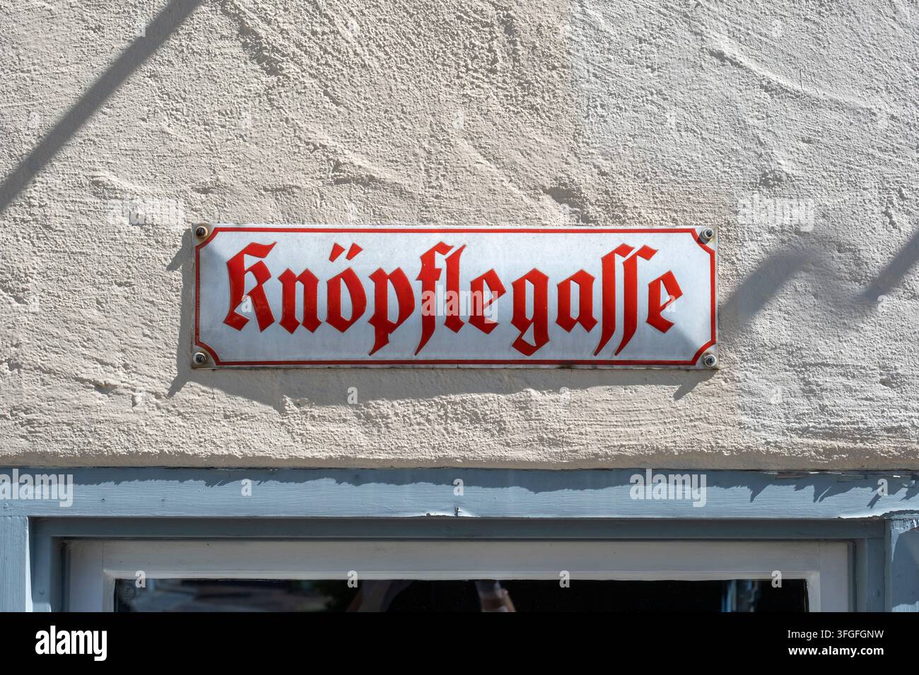 Segnale stradale storico per Knoepflegasse in classica lettera rossa a frattura su sfondo bianco con bordo decorato, montato su un muro di casa luminoso a Foto Stock
