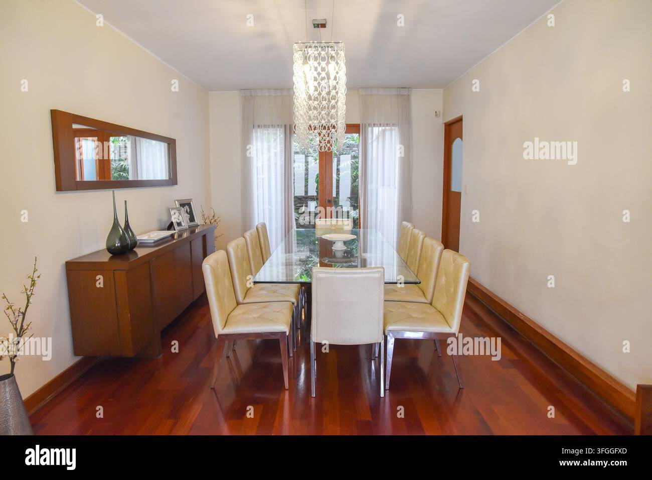Sala da pranzo elegante: Una sofisticata sala da pranzo presenta un lungo tavolo con piano in vetro circondato da sedie imbottite, illuminato da un moderno lampadario Foto Stock