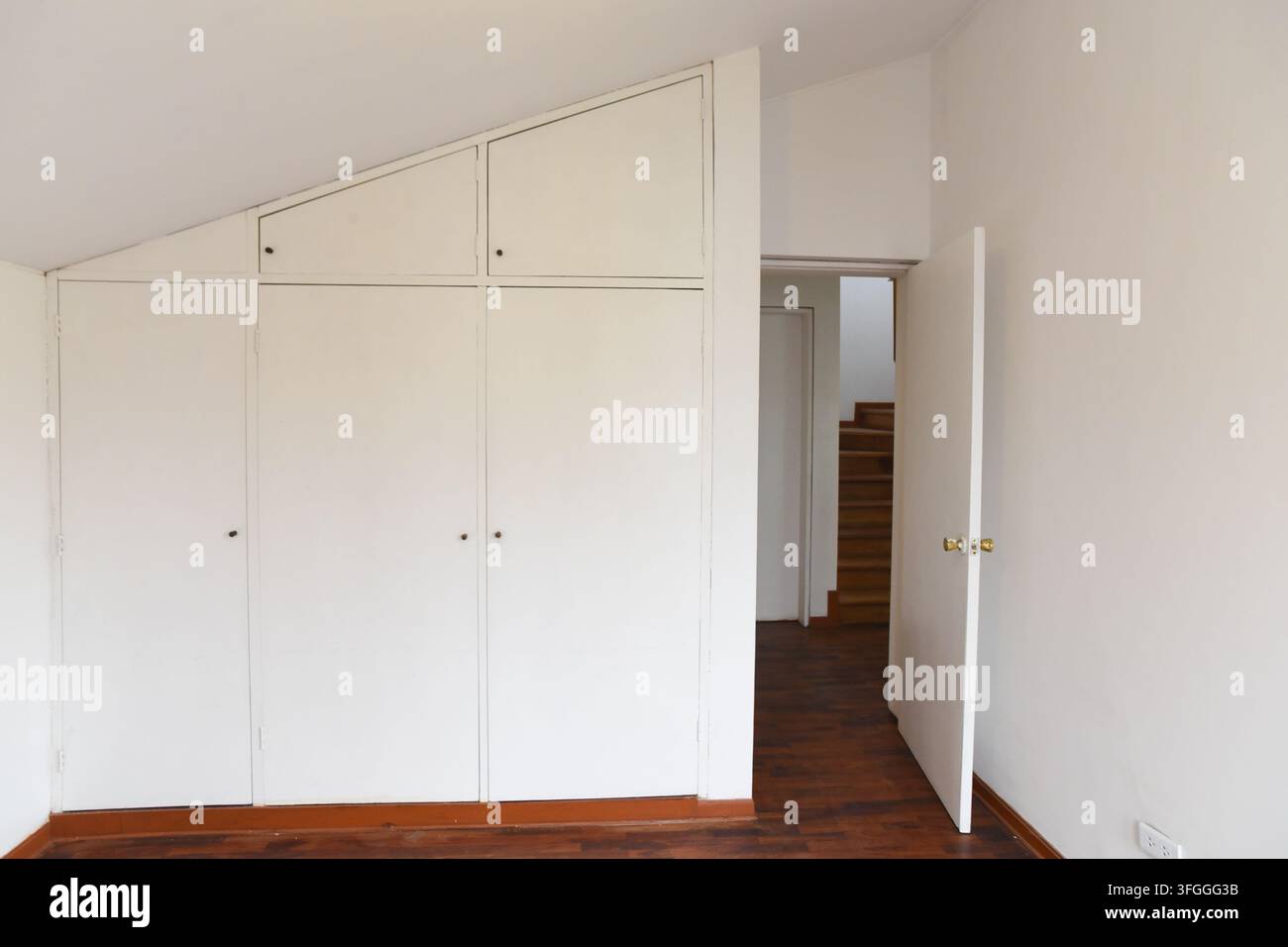 Soluzioni di archiviazione per soffitte: Uno spazio di soffitta pulito e luminoso con armadi bianchi incorporati e un'anteprima di una scala che porta a un altro livello Foto Stock