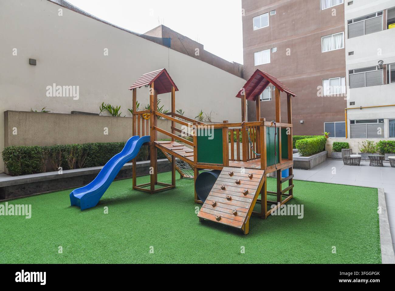 Parco giochi moderno: Uno scivolo di plastica colorato e una struttura di arrampicata in legno offrono uno spazio ricreativo divertente per i bambini Foto Stock