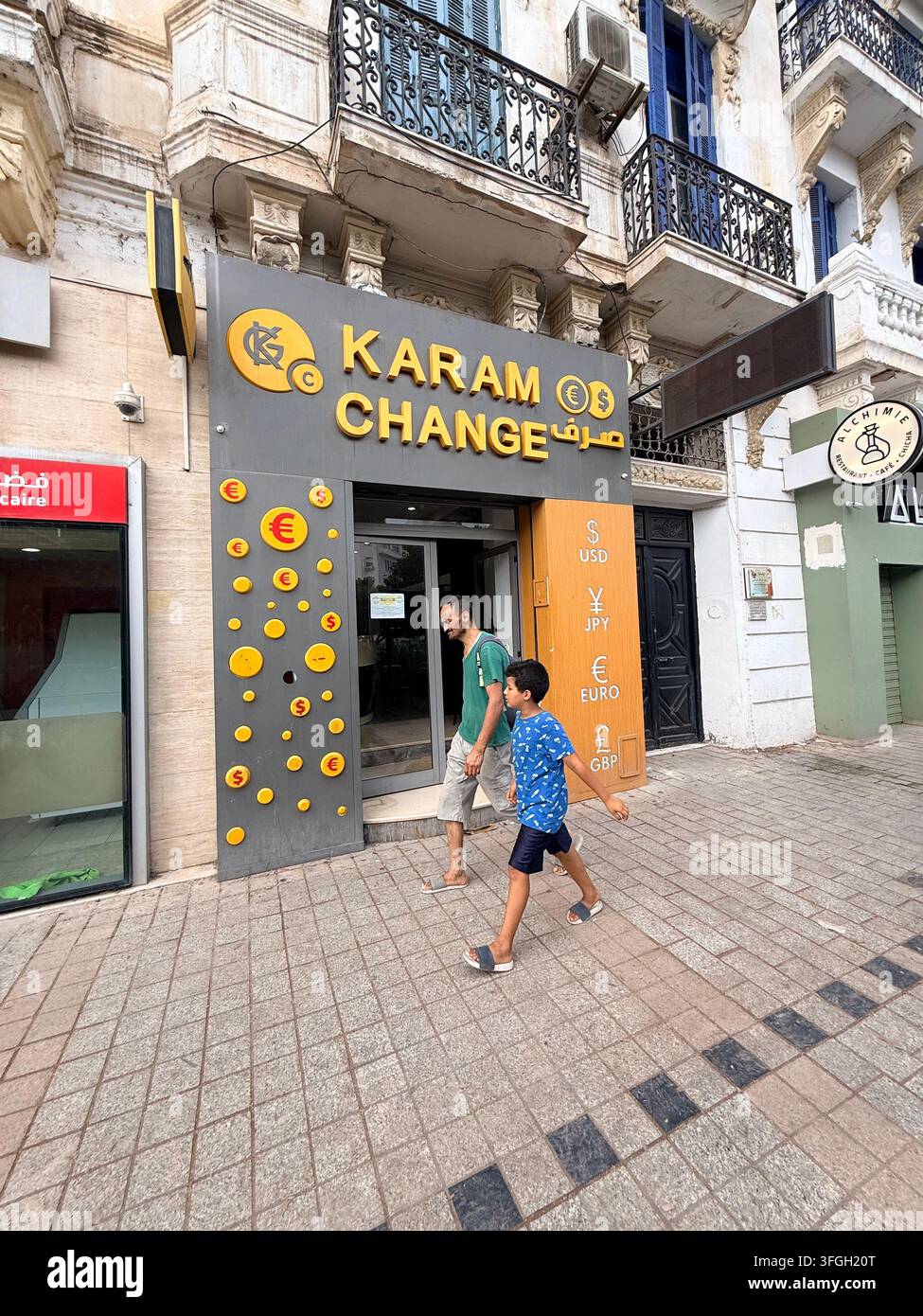 Pedoni davanti a un ufficio di cambio valuta a Tunisi, Tunisia, con cartelli in arabo e simboli del dollaro USA e dell'euro - Immagine stock catturata con smartphone