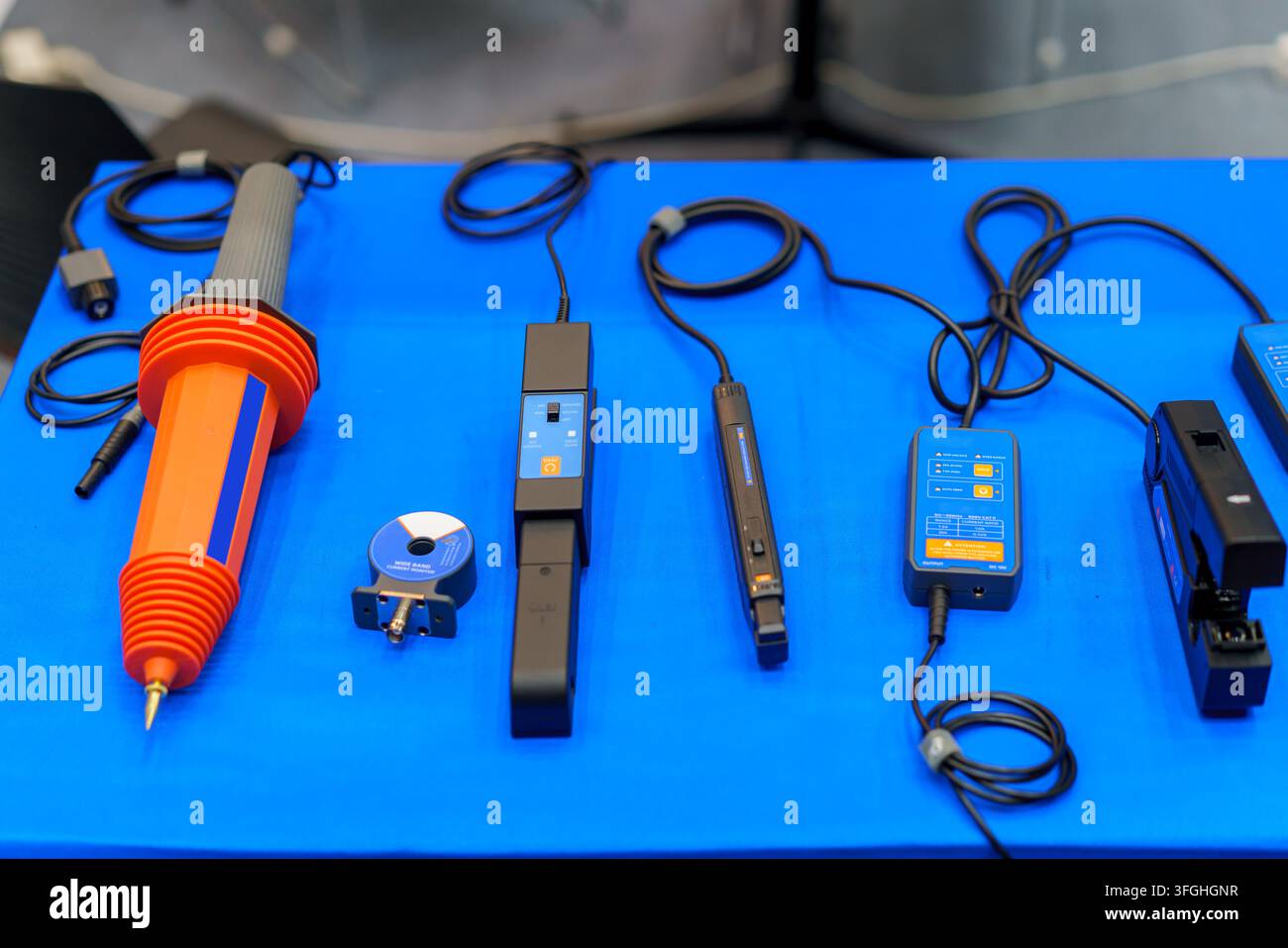 Una collezione di apparecchiature per test elettrici, inclusa una sonda ad alta tensione e vari sensori di corrente a morsetto, visualizzati su una superficie blu per ind Foto Stock