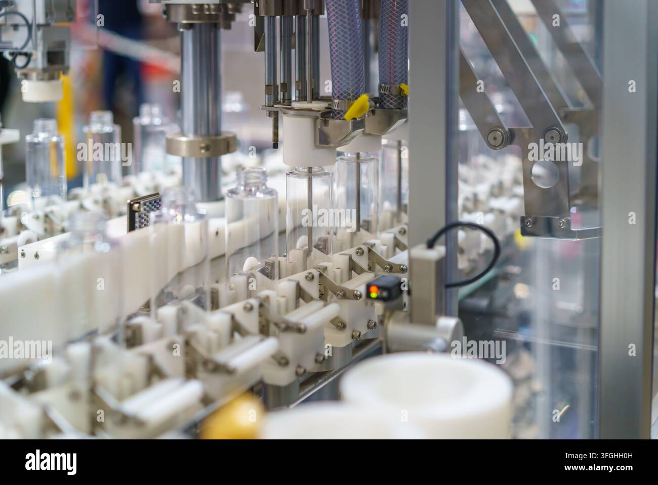 Primo piano di una macchina industriale automatizzata che elabora bottiglie di plastica trasparente su una linea di produzione moderna. L'attrezzatura utilizza ugelli precisi Foto Stock