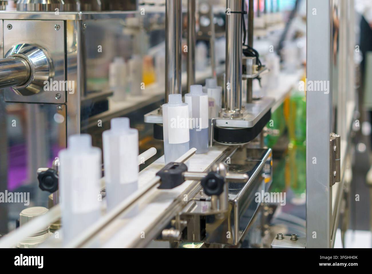 Primo piano di bottiglie di plastica bianca che si muovono lungo un nastro trasportatore in acciaio inossidabile su una macchina automatica per il riempimento e l'imballaggio industriale in una moderna fa Foto Stock