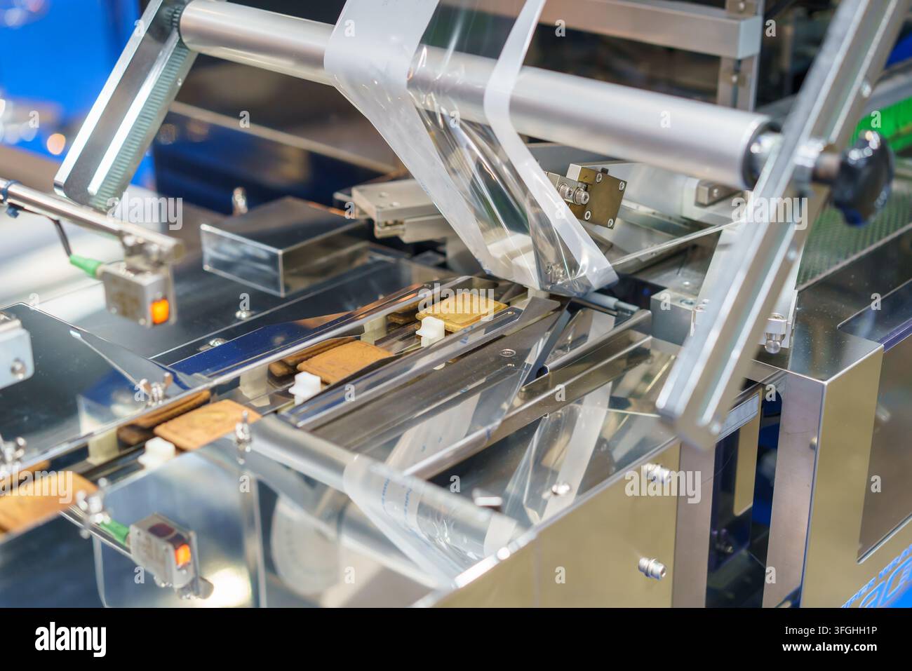 Prima di una macchina industriale di incartamento a flusso che sigilla biscotti quadrati in pellicola di plastica trasparente su una linea di produzione automatizzata in acciaio inossidabile. Foto Stock