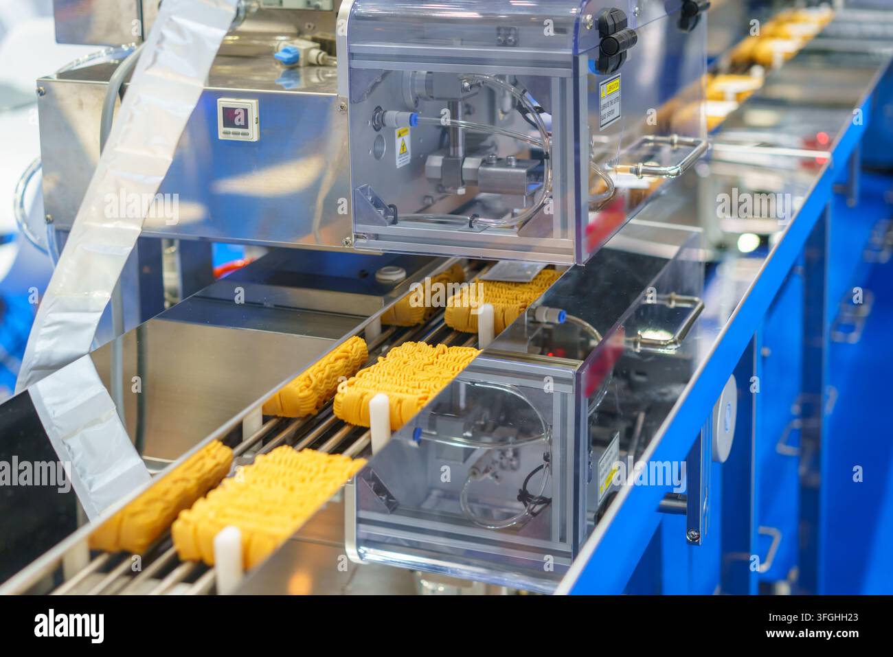 Blocchi di noodles istantanei essiccati che avanzano su un nastro trasportatore attraverso una macchina di confezionamento automatizzata in un moderno stabilimento di produzione alimentare. Foto Stock