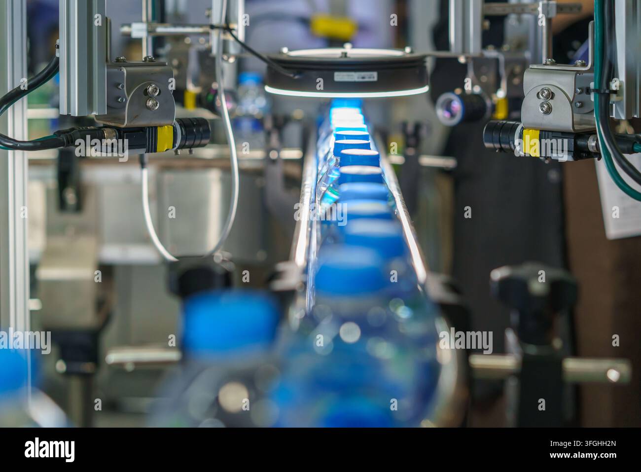 Prima piano di una macchina per l'etichettatura automatica che applica etichette di carta bianca su bottiglie di plastica che avanzano su un nastro trasportatore in un moderno stabilimento di produzione. Foto Stock