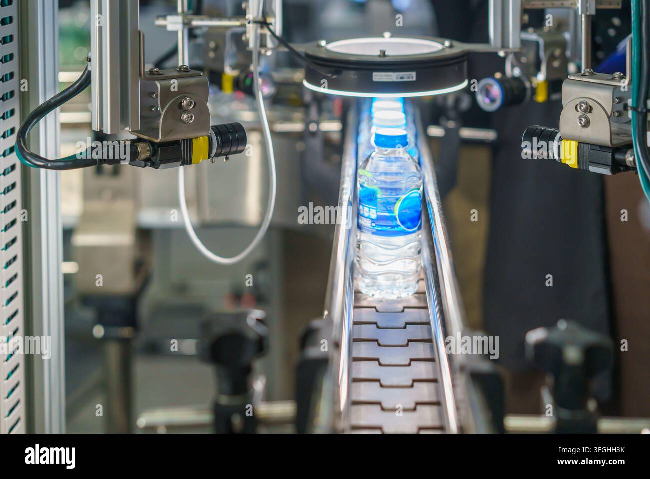 Primo piano di una linea di produzione automatizzata con bottiglie d'acqua di plastica. Un sistema di visione meccanica con una luce intensa ispeziona una bottiglia per il controllo qualità Foto Stock