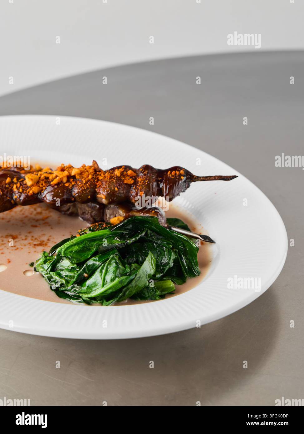 Spiedino grigliato ad alto contenuto proteico con spinaci appassiti e crumble di noci per una consistenza croccante, presentazione pulita ideale per la preparazione di pasti fitness Foto Stock