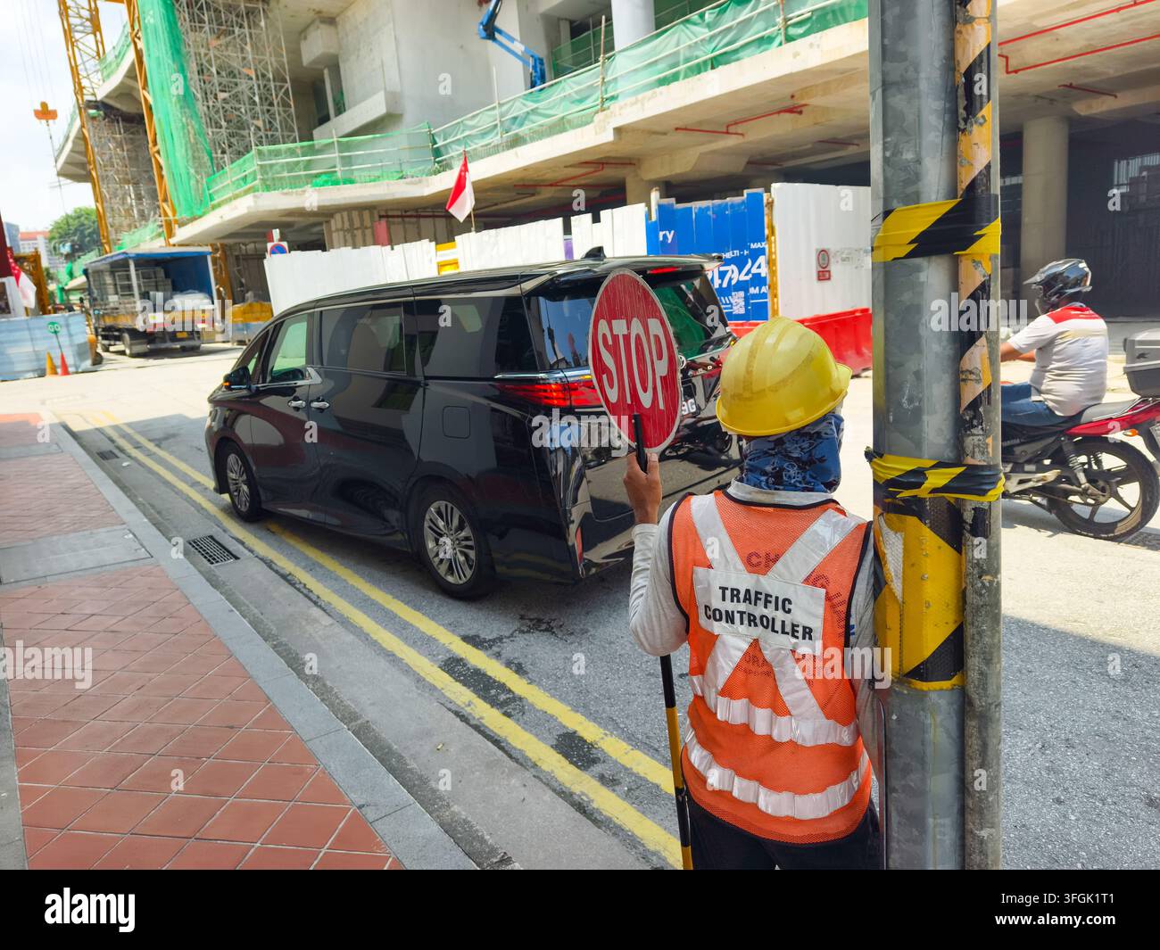 Controllore del traffico in cantiere che indossa un giubbotto ad alta visibilità e un casco di sicurezza, tiene un cartello rosso "STOP" per regolare il traffico stradale, Singapore Foto Stock