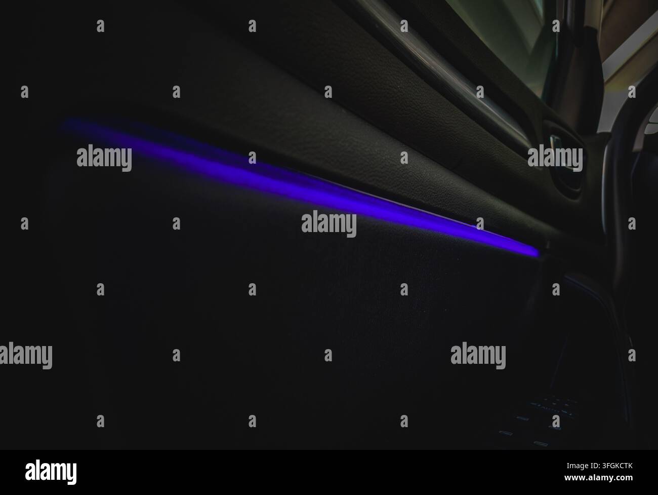 Primo piano del pannello interno della porta dell'interno moderno dell'auto con striscia luminosa LED ambientale viola brillante in una cabina buia di notte. Foto Stock