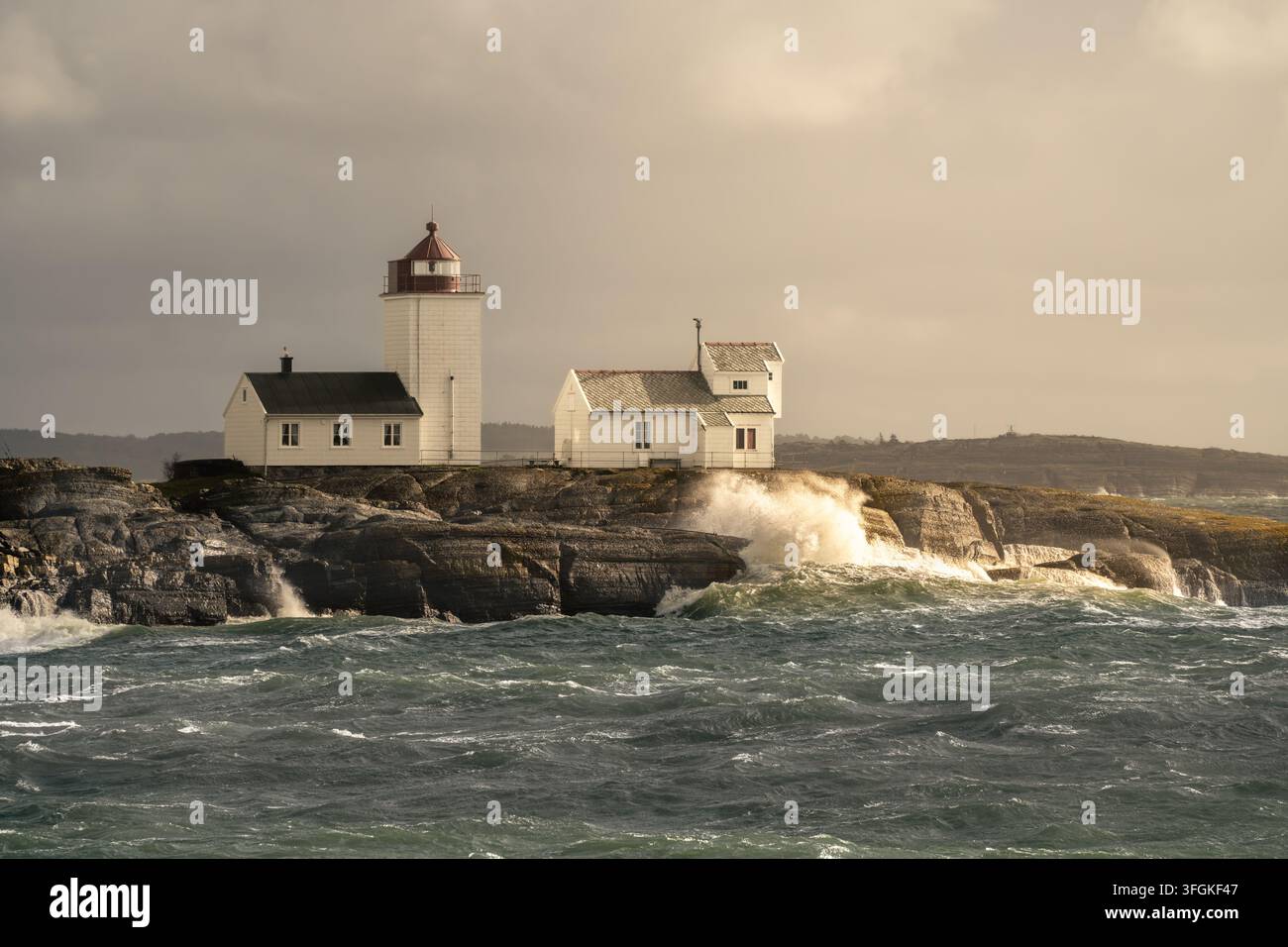 L'illuminazione costiera transitoria riscalda il faro di Langoytangen e gli spruzzi d'acqua mentre l'acqua scura si muove sotto in Norvegia per il tempo mutevole, atmosfera marittima Foto Stock